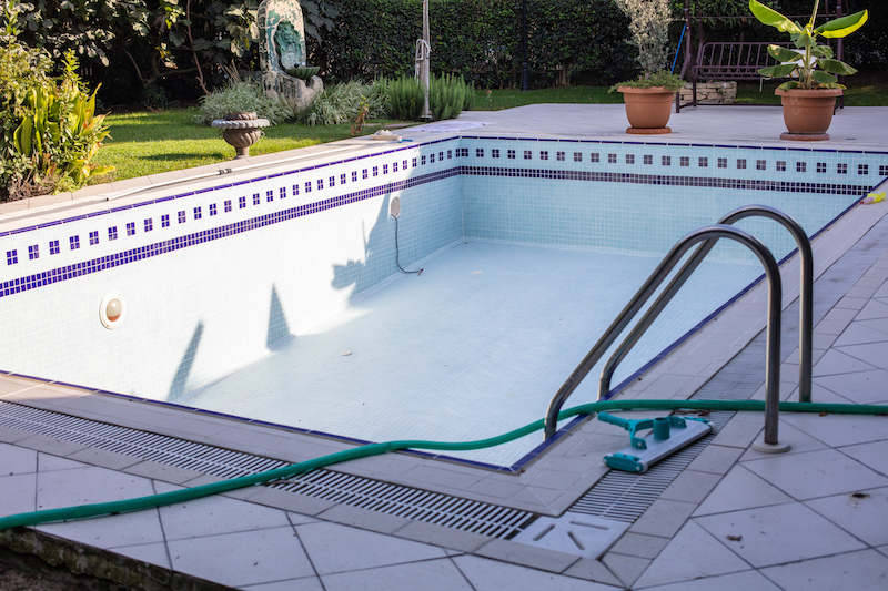 Swimming pool that is almost empty with dirty water end of the summer season