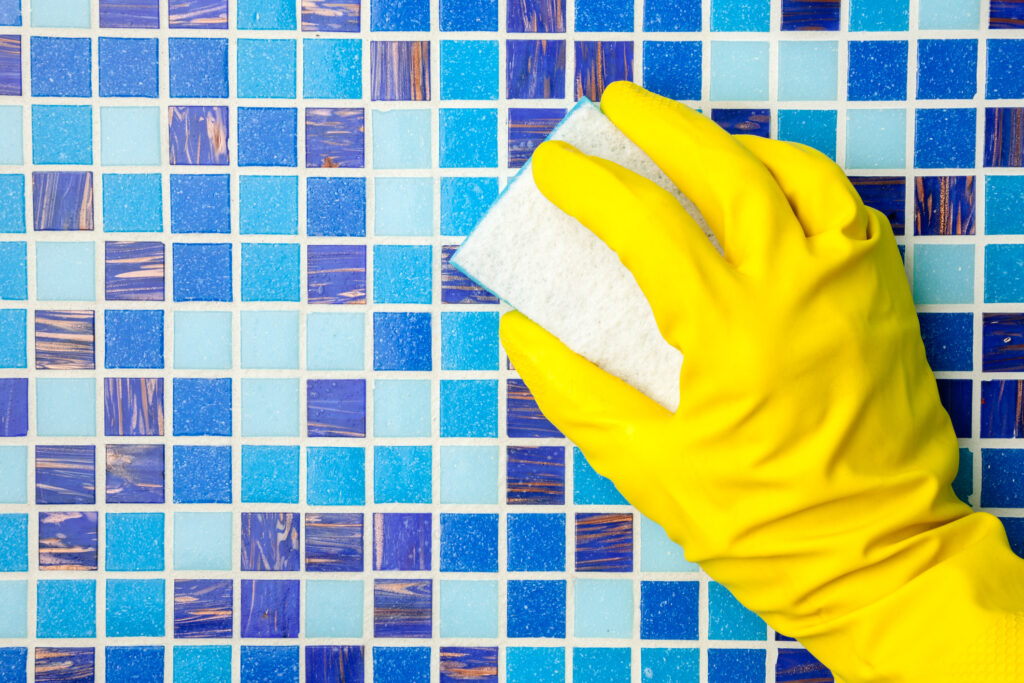 Hand in yellow protective glove cleaning mosaic pool wall