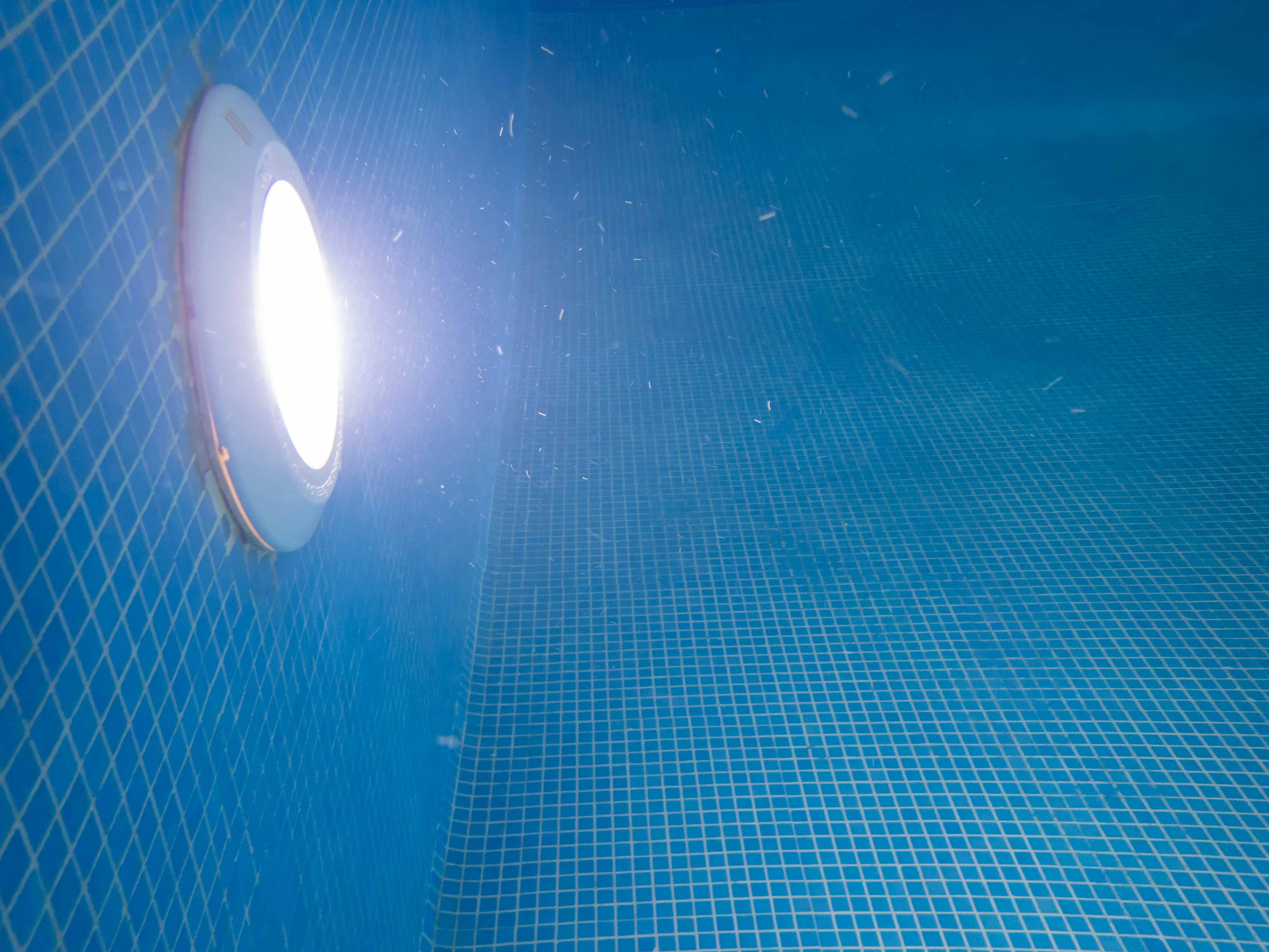 Underwater view of blue mosaic tile swimming pool interior with decorative tile and light